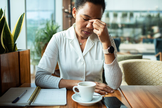 Stressed healthcare worker rubbing eyes during coffee break at cafe
