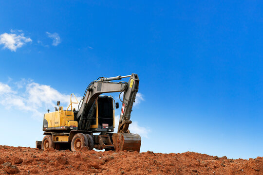 Yellow excavator on dirt mound under blue sky at construction site with copy space