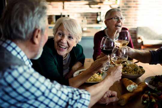 Senior friends toasting with wine at home dinner table