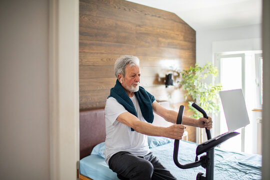Senior man cycling on exercise bike in bedroom at home