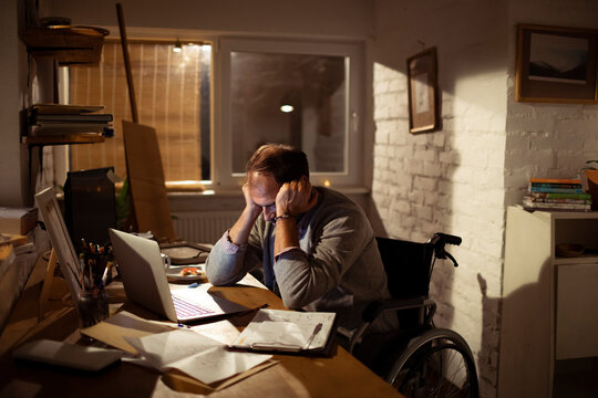 Stressed man in wheelchair working late at home office
