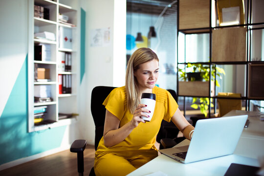 Young woman working on laptop with coffee in modern office