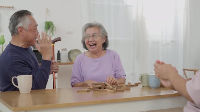 Asian senior man with friends playing wooden block tower game with concentration during indoor leisure activity. Active retirement lifestyle and wellness concept	
