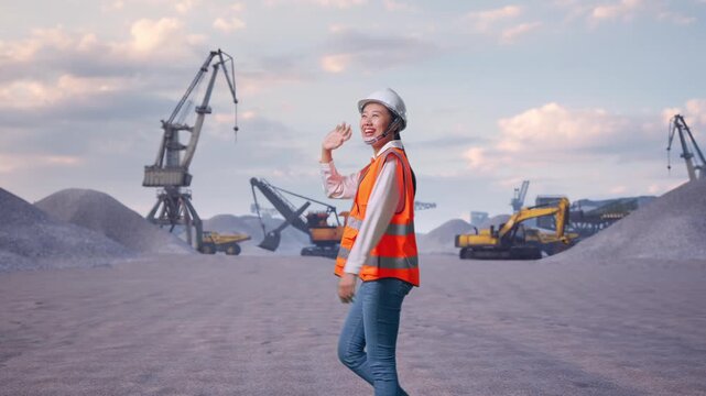 Side View of Asian Female Engineer Waving Hand Saying Bye While Walking at Gravel Stockpile Yard with Cranes and Excavators