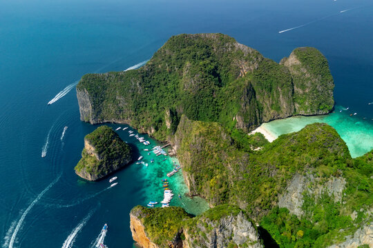 Boats navigate around the limestone cliffs of Maya Bay on Phi Phi Leh island during a bright sunny day in Thailand as tourists visit the tropical coast