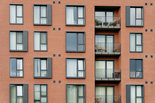 A tight view of a red brick apartment facade shows dark window frames, planted balconies and the anchor plates that reveal how the rainscreen is actually built.