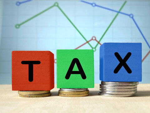 TAX blocks positioned on coins against financial charts, representing taxation, government revenue, financial planning and economic analysis.