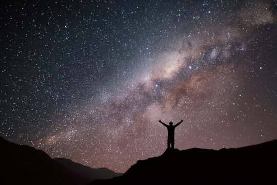Silhouette of a person standing on a mountain peak looking at the milky way galaxy and starry night sky with milkyway silhouette mountain astronomy stargazing universe exploration
