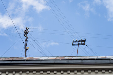 Overhead power lines fan out from two roof-mounted poles above an old cornice, legacy electrical distribution still strung right across the rooftops here. © K