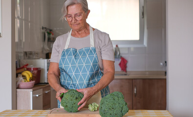 Senior woman preparing fresh broccoli in a home kitchen, actively engaging in healthy cooking for a...