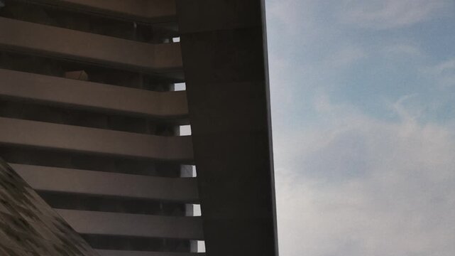 A section of a modern building is visible, showing concrete lines and beams. The sky is clear with some clouds. This view captures architecture in an urban area.