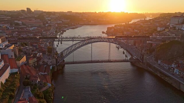 Drone view of Porto, Portugal, at sunset with a tram on Dom Luis I Bridge, Porto Ribeira, Vila Nova de Gaia, and sunset light. Push in approach dolly shot