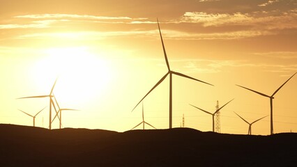 sunset silhouette of wind turbines generating green energy © zhu difeng