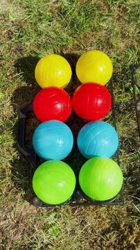 Vertical video social media - A man&rsquo;s hands laying down a carrier of colorful weighted plastic bocce or boules balls, outside on grass, then throwing in a small white jack ball, ready to play a game.