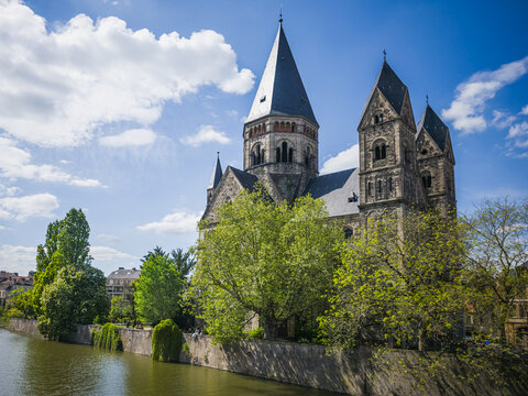 Metz, France &ndash; April 26, 2025: View of the historic Temple Neuf Protestant church standing on the banks of the Moselle River in Metz. The Romanesque Revival landmark is surrounded by spring greenery u