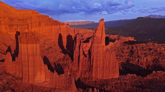 Sweeping sunset flight reveals towering Cutler sandstone Fisher Towers spires and rugged desert canyons bathed in warm evening light near Moab Utah