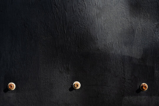 Black coated wood texture background with three rusty fasteners, rough finish and dark copy space