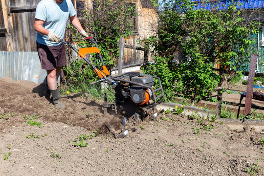 Gardener using motorized cultivator on the plantation. Plowing garden with a motor cultivator before planting potatoes and other crops