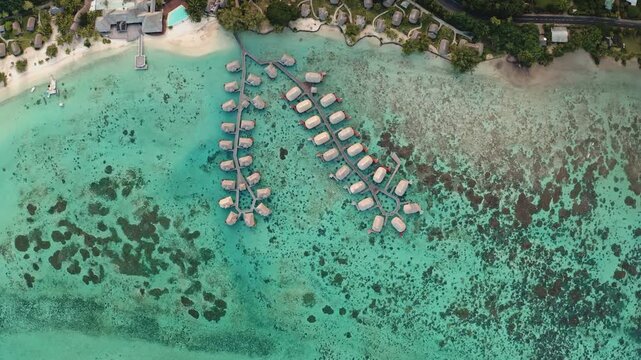 French Polynesia overwater bungalows in luxury resort stretching across vibrant turquoise lagoon, surrounded by coral reef and lush tropical vegetation, offering an idyllic travel and vacation escape