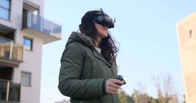 Female pilot wearing first person view goggles operates a motion controller to fly a drone, enjoying an immersive piloting experience