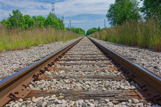 Low-angle view of railroad tracks stretching into a lush green countryside, emphasizing perspective, vanishing point and textured wooden ties with and open sky. in Plymouth, IN