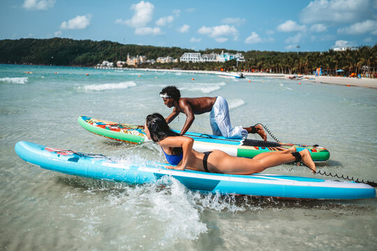 Young multiethnic people, couple having fun on surfboards in the clear ocean water during summer