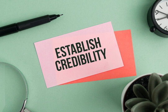 Magnifying glass and colored paper with the words ESTABLISH CREDIBILITY. The concept of credibility.