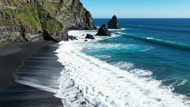 Coastal seascape with waves crashing on black sand beach and cliffs