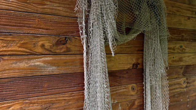 Fishing net hanging against rustic wooden wall, creating a maritime and nautical textured background, symbolizing traditional fishing culture and coastal living