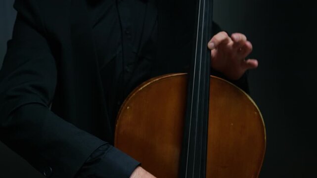Young adult Caucasian man playing cello, camera tilting up from hands bowing strings to his face. Footage is perfect for classical music concert promotions or music academy advertisements