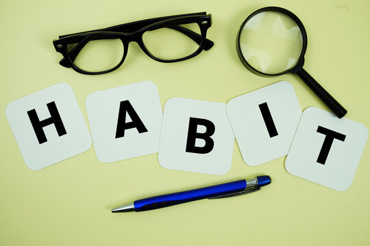 HABIT alphabet letters with magnifying glass, eye glasses and pen on yellow background