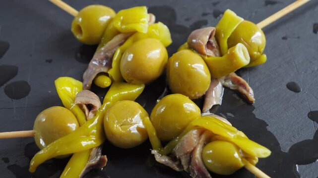 Close-up of traditional Spanish Gilda pintxos with green olives, anchovies and pickled peppers on skewers. High quality 4k footage