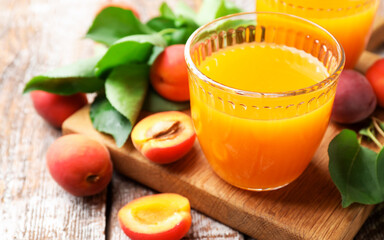 Glasses of tasty apricot juice, fresh fruits and leaves on wooden table, closeup © New Africa
