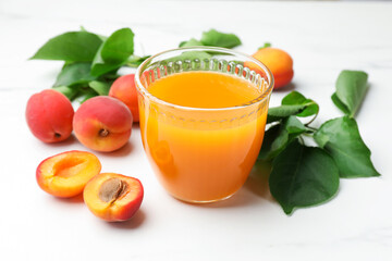 Glass of apricot juice, fresh apricots and leaves on white table, closeup © New Africa