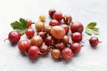 Fresh red gooseberries and green leaves on grey table, closeup © New Africa