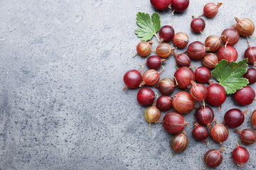 Fresh red gooseberries and green leaves on grey table, flat lay. Space for text © New Africa