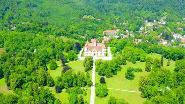 Graz, Austria. Eggenberg Palace, a Baroque masterpiece with four corner towers and red roofs, Drone footage over the expansive palace park and surrounding forested hills. Drone footage, Departure of 