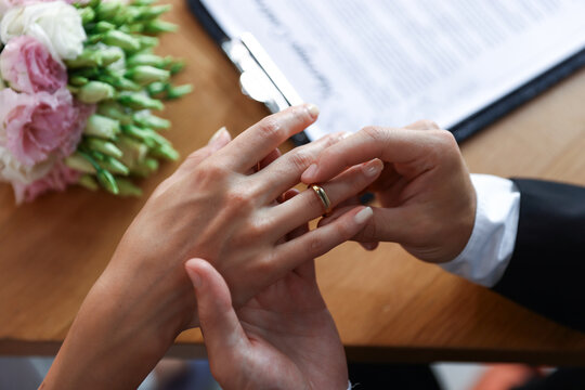 Man putting engagement ring on his girlfriend's finger at wooden table, closeup