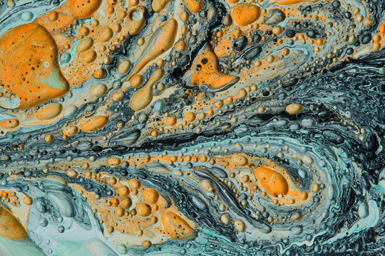 Abstract fluid art background with rich yellow bubbles floating on dark teal and grey marble waves.