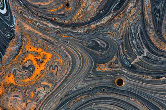Abstract black and vibrant orange fluid paint swirling pattern with cells and fluid motion.