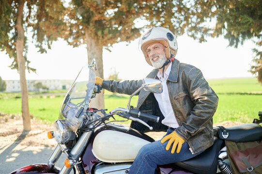 Happy senior biker wearing helmet and leather jacket is sitting on his motorcycle