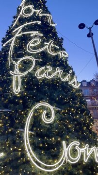 giant Christmas tree in Paris illuminated with neon lettering lights in front of a blue evening sky creating a festive holiday atmosphere