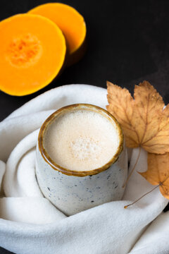 Pumpkin latte in scarf with fall leaves and pumpkin. Warm beverage during cold weather