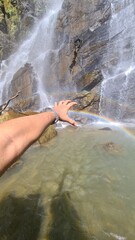 Obraz premium A person's hand reaching out to touch a beautiful rainbow created by a cascading waterfall in a natural landscape