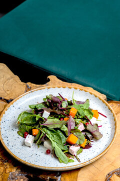 Plate with salad with greens, pumpkin and cheese on cafeteria table
