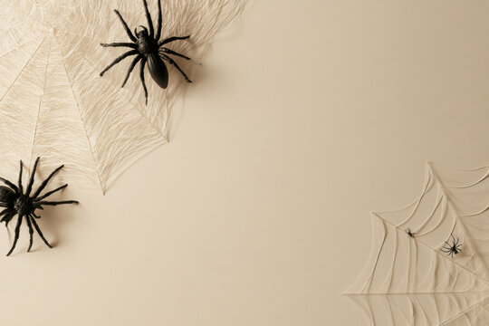 Minimalist halloween flat lay with plastic spiders and white webs on beige background with copy space