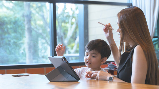 Mother guiding her young son while using a digital tablet together at a cafe