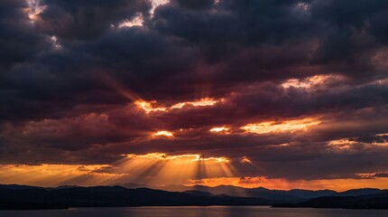 Fototapeta premium Dramatic Sunset Sky with Sunbeams Bursting Through Dark Storm Clouds Over Mountains and Water