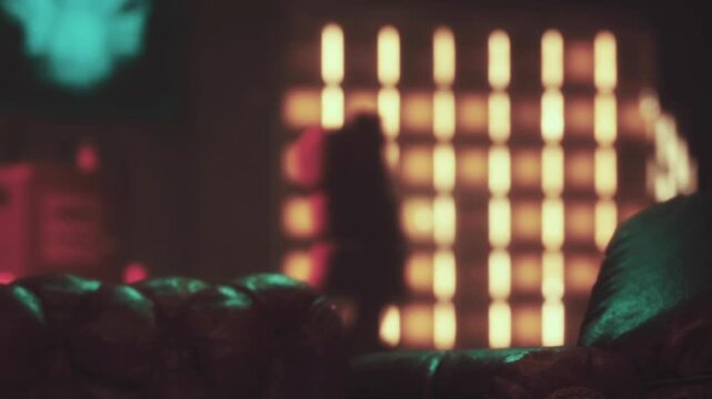 A soft brown couch sits in a well lit room. Colored lights create patterns on the wall. The scene has a relaxed atmosphere. There are shadows and warm tones in the background.