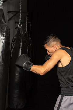 Young Hispanic boxer punching heavy bag during training in boxing gym